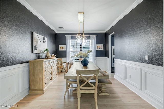dining space with an inviting chandelier, a textured wall, ornamental molding, and light wood finished floors
