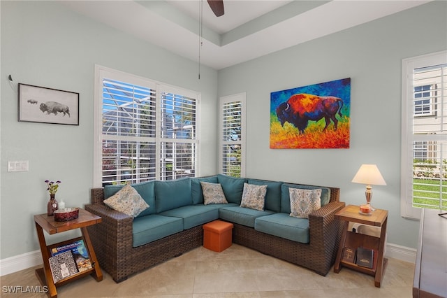 living area featuring baseboards, light tile patterned floors, a tray ceiling, and a ceiling fan