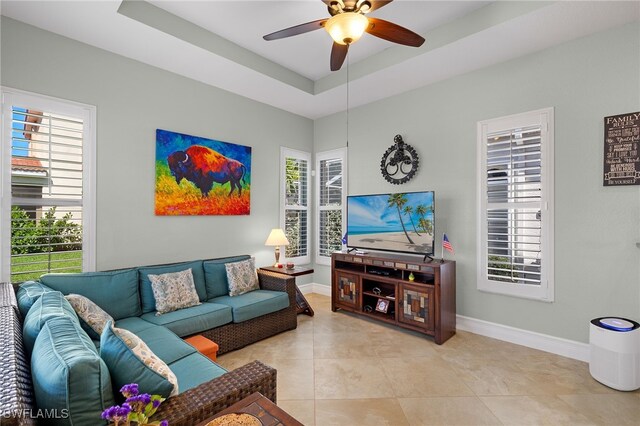 living area with baseboards, a tray ceiling, light tile patterned flooring, and a ceiling fan