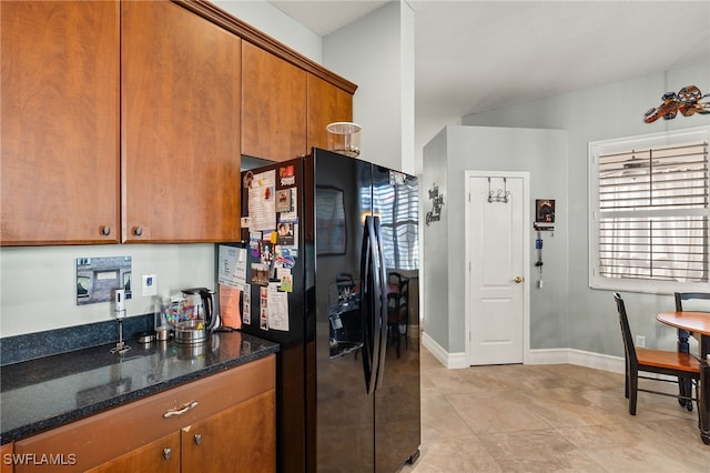 kitchen with brown cabinets, baseboards, dark stone countertops, and black fridge