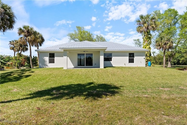 rear view of property featuring stucco siding, a yard, and metal roof