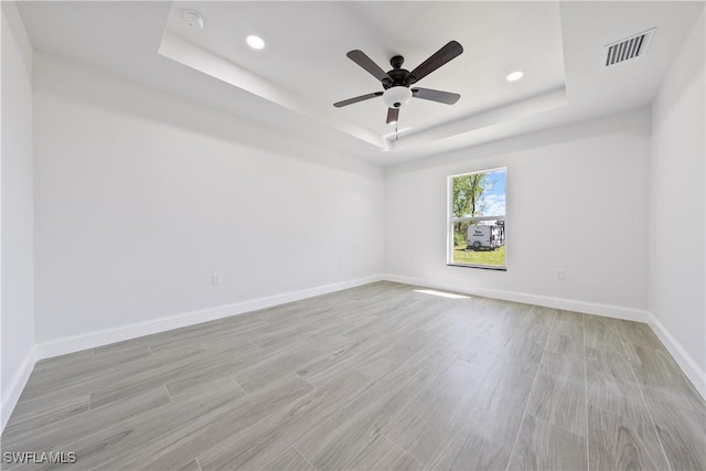 unfurnished room with a tray ceiling, light wood-type flooring, baseboards, visible vents, and ceiling fan