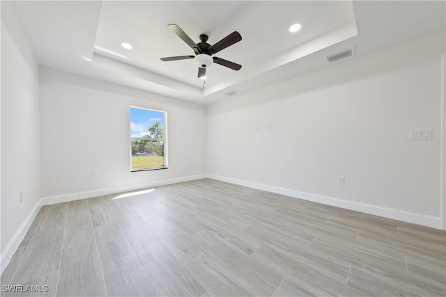 spare room with a tray ceiling, a ceiling fan, light wood-type flooring, baseboards, and recessed lighting