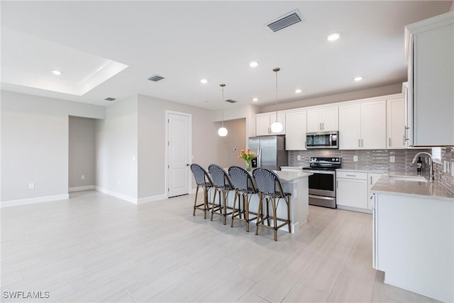 kitchen featuring visible vents, a kitchen bar, stainless steel appliances, a sink, and a center island