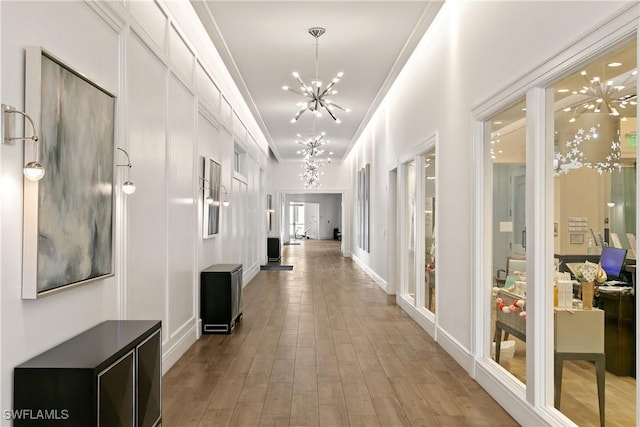 corridor with a notable chandelier, light wood-style flooring, and crown molding