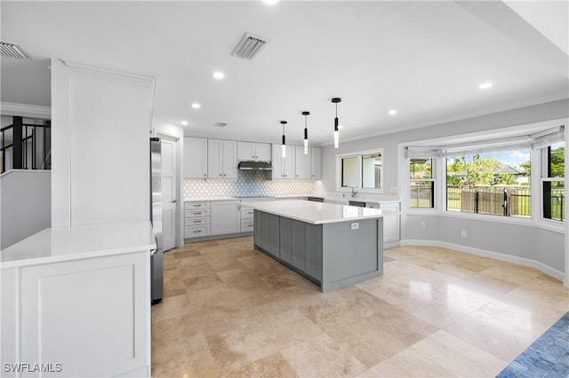 kitchen featuring light countertops, backsplash, a center island, under cabinet range hood, and visible vents
