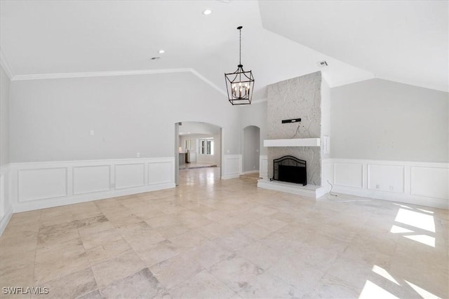 unfurnished living room featuring a notable chandelier, vaulted ceiling, a fireplace, a decorative wall, and arched walkways