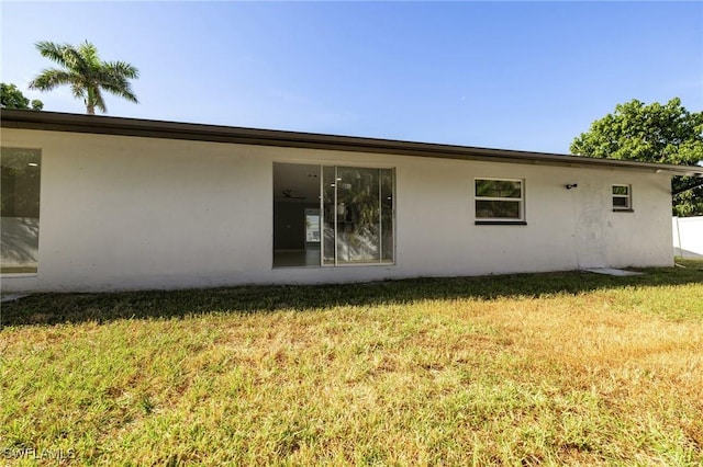 rear view of house featuring a lawn and stucco siding