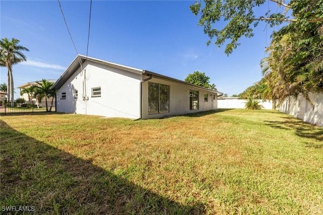 rear view of property featuring stucco siding, a yard, and a fenced backyard