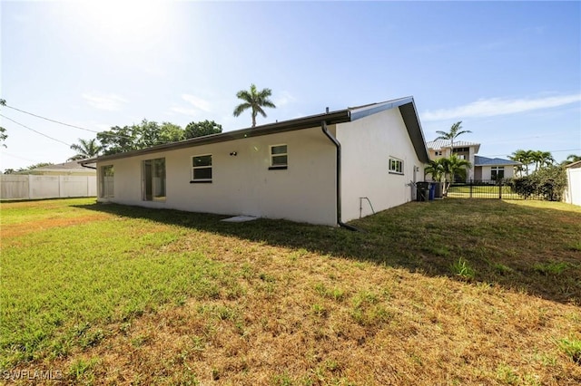 back of property featuring stucco siding, fence, and a yard