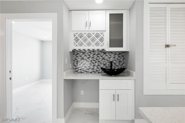 bar with marble finish floor, a sink, baseboards, decorative backsplash, and bar