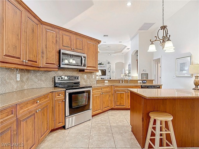 13011 Milford Pl, Fort Myers, FL 33913 - kitchen with a kitchen breakfast bar, stainless steel appliances, light tile patterned flooring, a peninsula, and brown cabinets