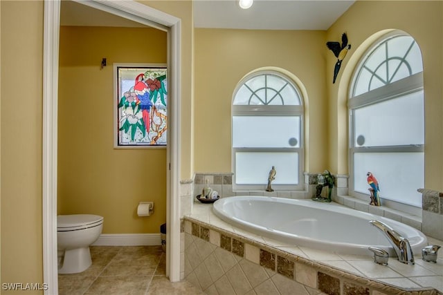 bathroom with tile patterned floors, toilet, baseboards, and a bath