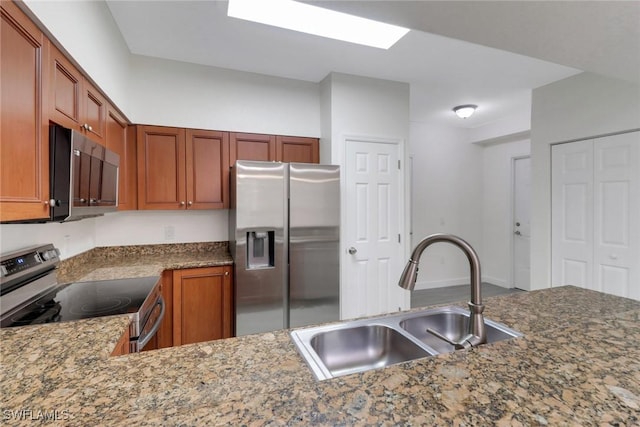 kitchen with stainless steel appliances, brown cabinets, a sink, and dark stone countertops