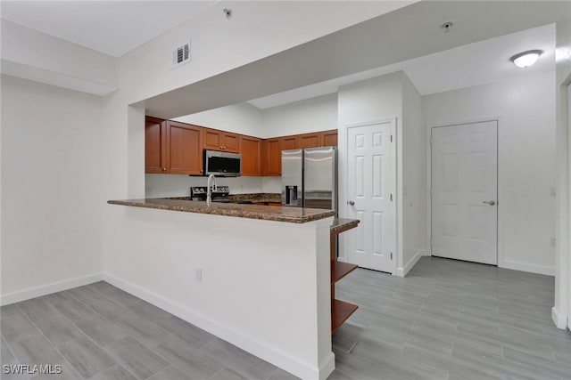 kitchen featuring baseboards, a peninsula, visible vents, brown cabinetry, and appliances with stainless steel finishes