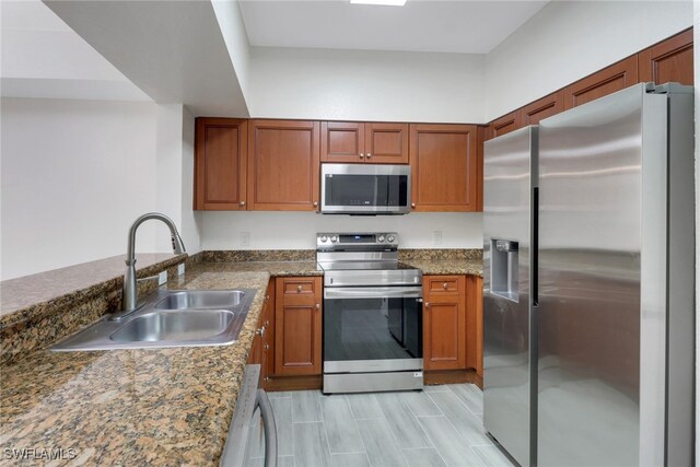 kitchen with dark stone countertops, brown cabinets, a sink, and stainless steel appliances