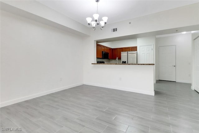 unfurnished living room with visible vents, baseboards, an inviting chandelier, a sink, and light wood finished floors
