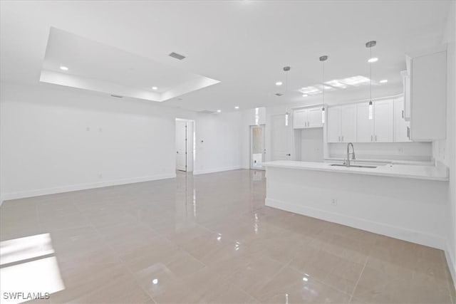 150 Bell Blvd S, Lehigh Acres, FL 33974 - kitchen with white cabinetry, light countertops, a tray ceiling, a sink, and a peninsula