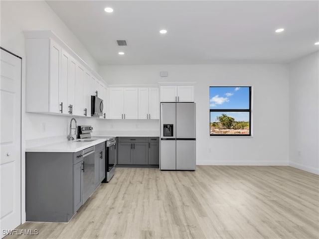 633 Cane St E, Lehigh Acres, FL 33974 - kitchen featuring appliances with stainless steel finishes, gray cabinetry, light wood-style flooring, a sink, and light countertops