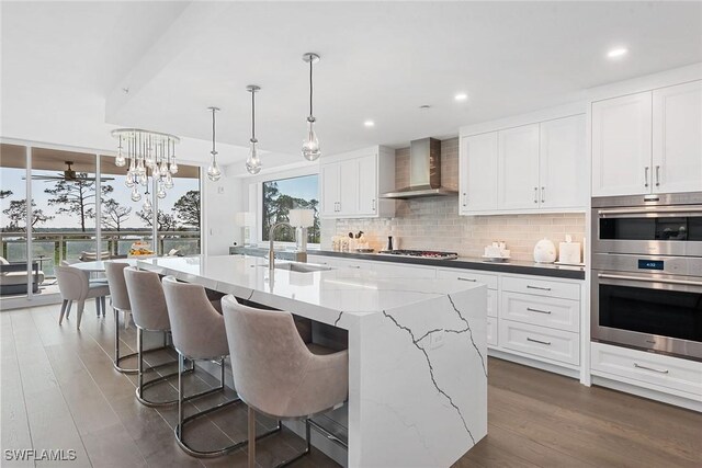 13945 Old Coast Rd Unit 406, Naples, FL 34110 - kitchen featuring wall chimney exhaust hood, stainless steel appliances, tasteful backsplash, dark wood-type flooring, and a sink