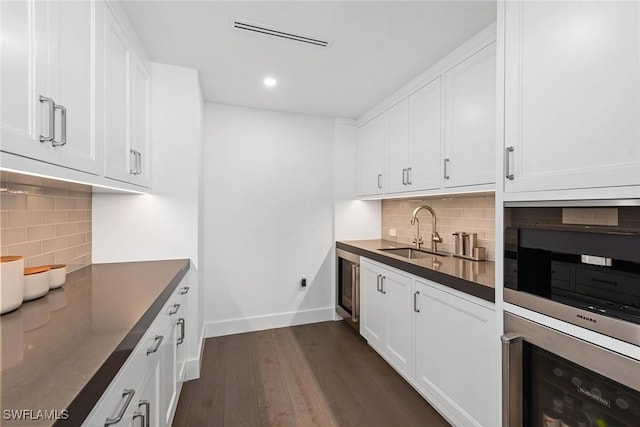 kitchen with a sink, beverage cooler, baseboards, dark countertops, and backsplash