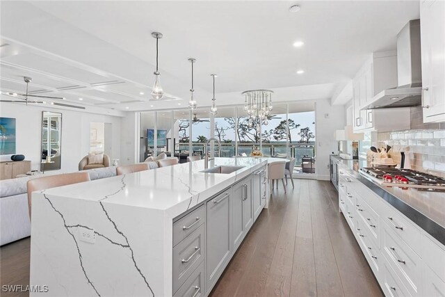 13945 Old Coast Rd Unit 406, Naples, FL 34110 - kitchen featuring wall chimney exhaust hood, a sink, open floor plan, stainless steel gas stovetop, and a center island with sink