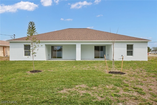 rear view of house featuring roof with shingles, stucco siding, and a yard