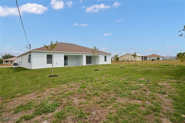 back of house with stucco siding and a yard