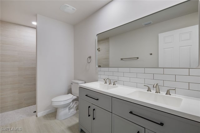 bathroom with a tile shower, tasteful backsplash, toilet, and a sink