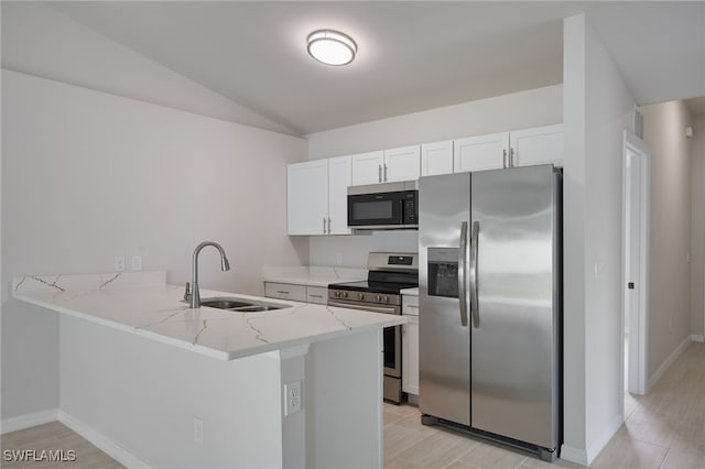 kitchen featuring a peninsula, light stone countertops, stainless steel appliances, lofted ceiling, and a sink