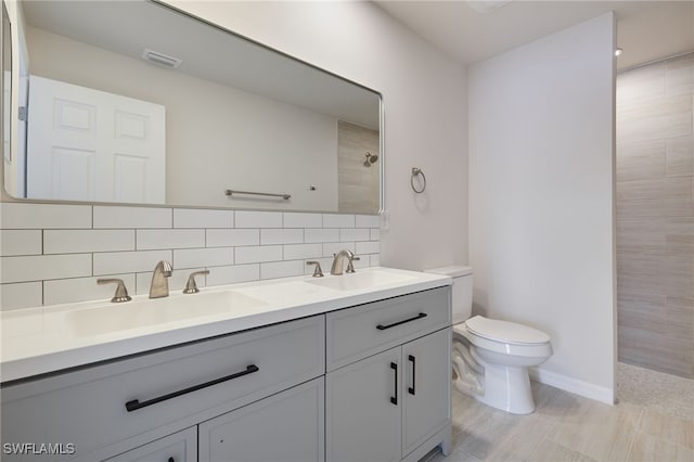 bathroom with backsplash, toilet, tiled shower, and a sink