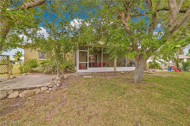 view of front of property with a front lawn, stucco siding, a sunroom, and a playground