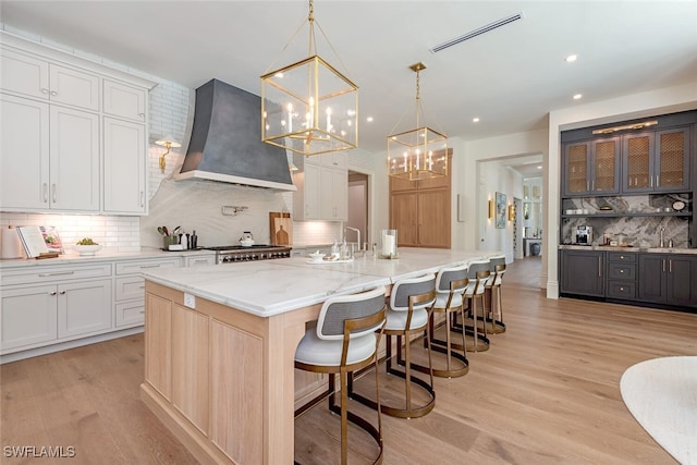 4300 Brynwood Dr, Naples, FL 34119 - kitchen with an inviting chandelier, wall chimney exhaust hood, white cabinetry, backsplash, and range