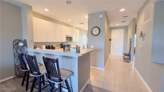 14512 Abaco Lakes Dr Unit 103, Fort Myers, FL 33908 - kitchen featuring a kitchen bar, light countertops, stainless steel microwave, light tile patterned floors, and white cabinets