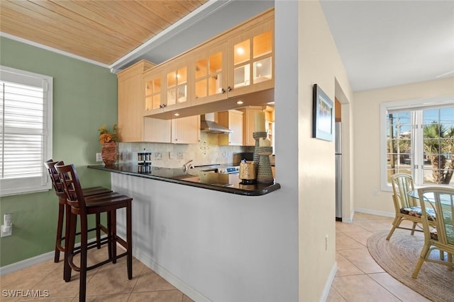 kitchen with freestanding refrigerator, light tile patterned floors, tasteful backsplash, and wall chimney exhaust hood