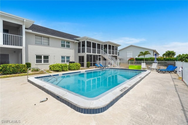 community pool with a patio area, a sunroom, and fence