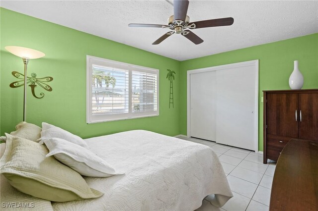 bedroom featuring a ceiling fan, light tile patterned floors, a closet, and a textured ceiling