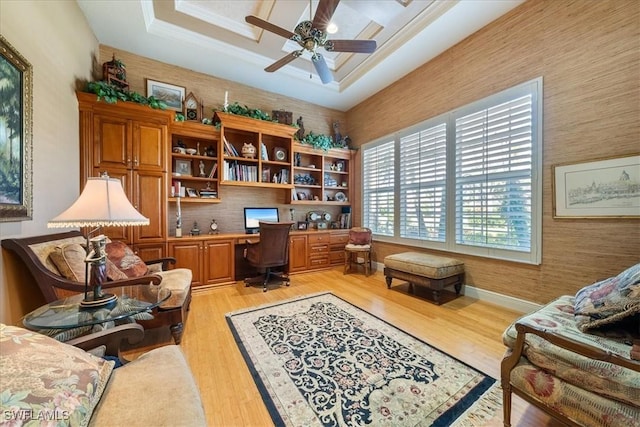 office featuring crown molding, light wood-type flooring, a ceiling fan, built in desk, and baseboards