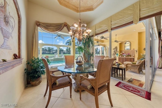 dining area with a raised ceiling, crown molding, ceiling fan with notable chandelier, and light tile patterned floors