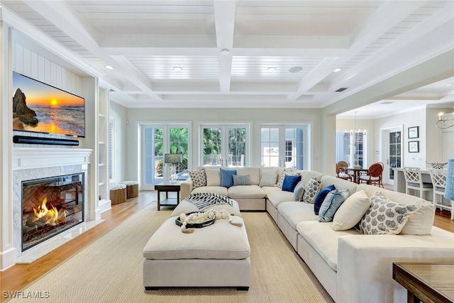 living area featuring an inviting chandelier, beam ceiling, light wood finished floors, a premium fireplace, and coffered ceiling