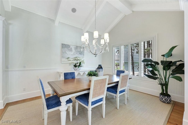dining space with a wainscoted wall, light wood-type flooring, beam ceiling, and a chandelier