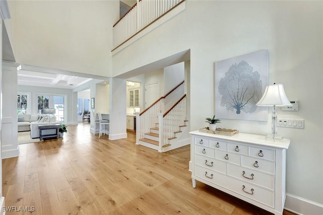 entryway featuring stairway, baseboards, light wood finished floors, and beam ceiling