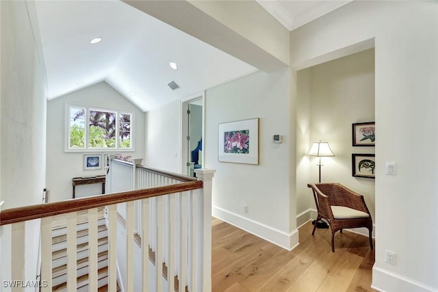 hallway with visible vents, lofted ceiling, light wood-style floors, baseboards, and an upstairs landing