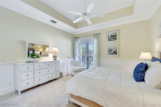bedroom with crown molding, light carpet, a wainscoted wall, a tray ceiling, and visible vents