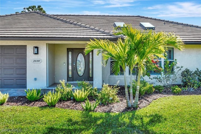 28389 Verde Ln, Bonita Springs, FL 34135 - doorway to property with an attached garage, stucco siding, a tiled roof, and a yard
