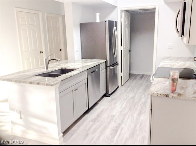 kitchen featuring a sink, appliances with stainless steel finishes, light stone countertops, and light wood-type flooring