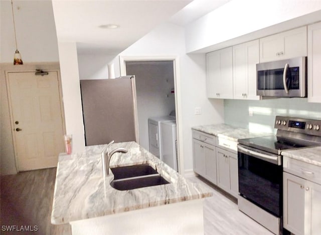 kitchen with washing machine and clothes dryer, stainless steel appliances, a sink, light wood-style floors, and light stone counters