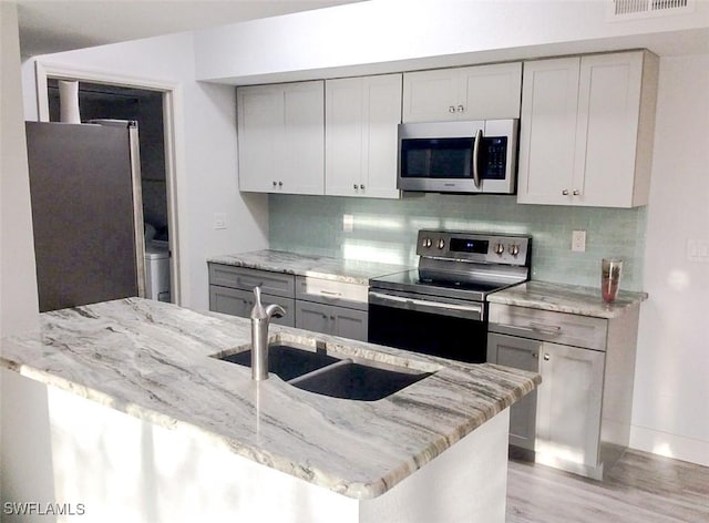 kitchen with decorative backsplash, light stone countertops, a sink, and stainless steel appliances