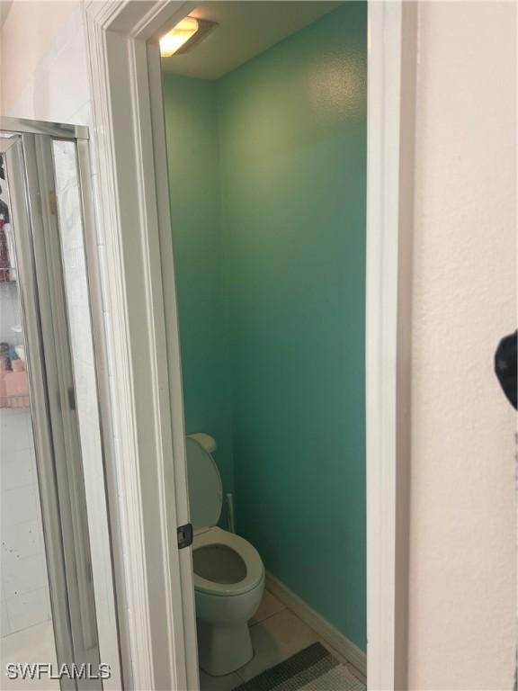bathroom with a stall shower, tile patterned floors, toilet, and baseboards