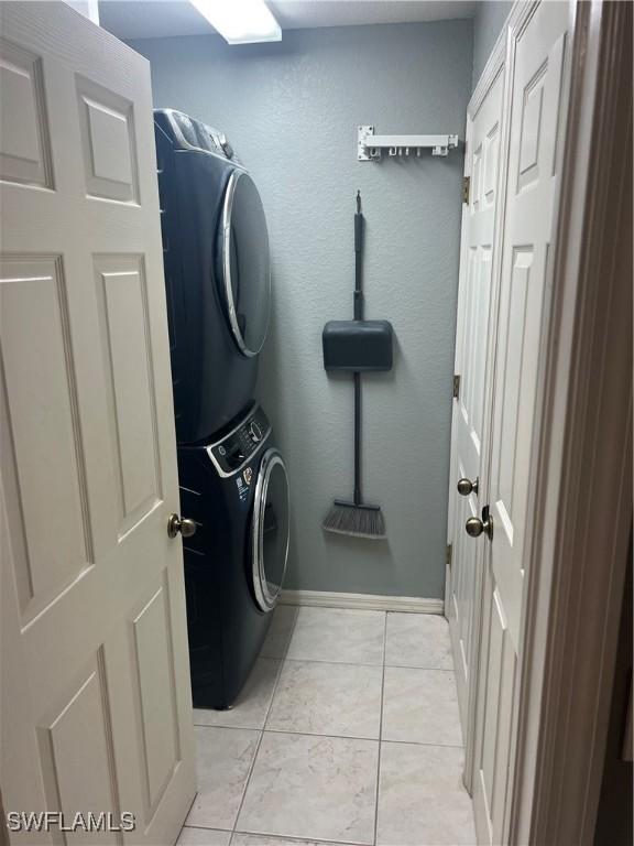 washroom with light tile patterned flooring, stacked washer and dryer, baseboards, and laundry area